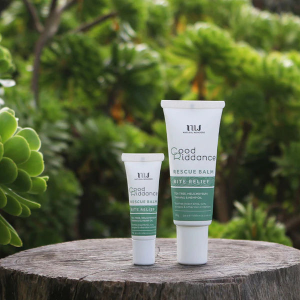 Two tubes of Good Riddance Rescue Balm on a wooden surface with a green leafy background