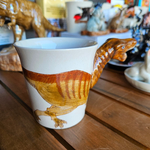 Ceramic mug with a dinosaur design on a wooden shelf.
