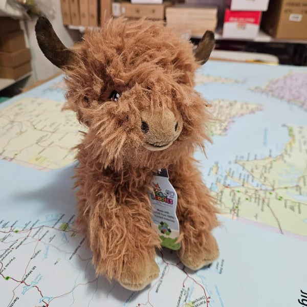 Plush toy highland cow on a map with shelves in the background