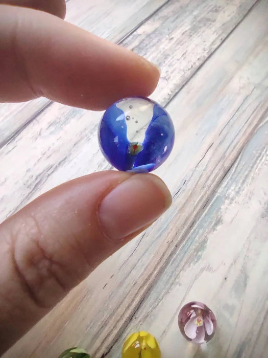 Blue glass marble with white swirl held between fingers, with colourful marbles below — Adventure Awaits