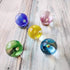 Five colourful glass marbles with flower-like swirls in blue, pink, yellow, green and aqua — Adventure Awaits
