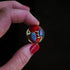 Hand holding a red glow-in-the-dark glass marble with blue and pink teardrop swirls, Adventure Awaits