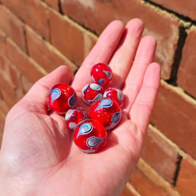 Hand holding six red glass marbles with colourful blue, green, pink and white swirls, Adventure Awaits