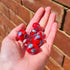 Hand holding six red glass marbles with colourful blue, green, pink and white swirls, Adventure Awaits