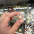 Hand holding a cream glass marble with red, blue and yellow flower-like swirls — Adventure Awaits