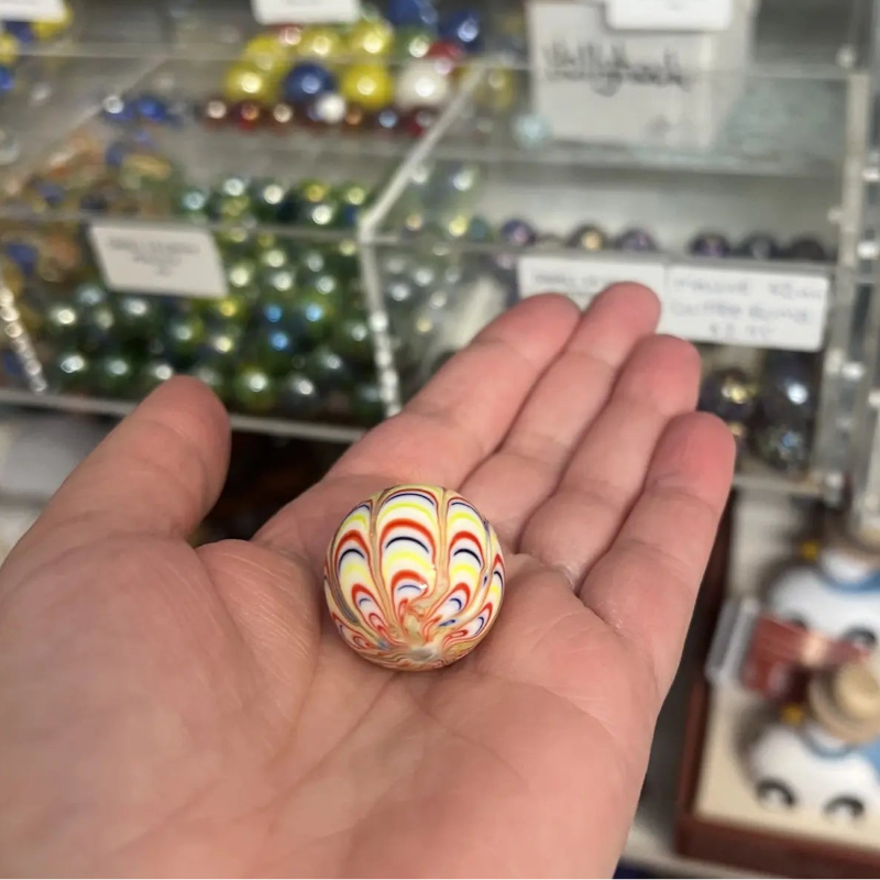 Colourful glass marble with red, yellow and blue swirls resting in an open hand — Adventure Awaits