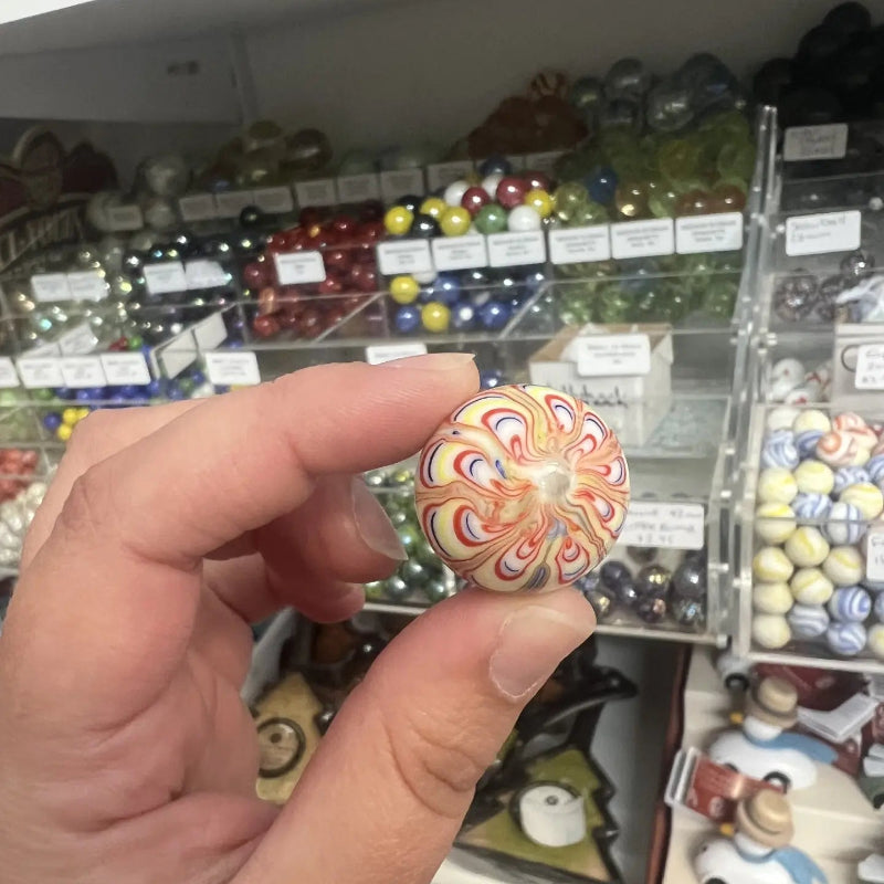 Hand holding a cream glass marble with red, blue and yellow flower-like swirls — Adventure Awaits