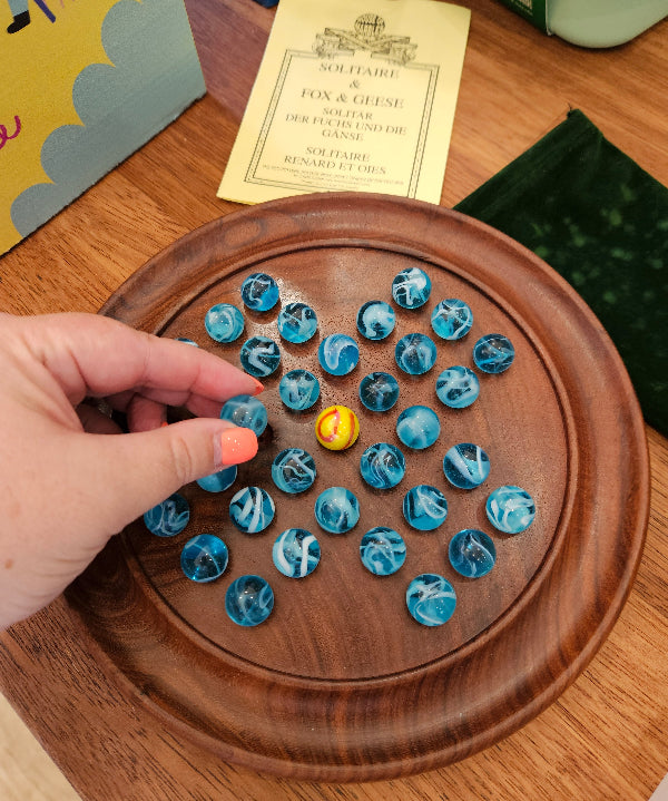 Wooden board game with blue and white pieces and a yellow piece, hand interacting with the game.
