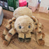 Plush huntsman spider toy on a wooden surface with a box and books in the background