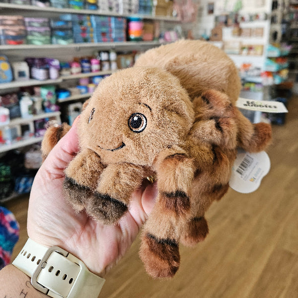 Plush toy huntsman spider held in a hand with a store shelf in the background