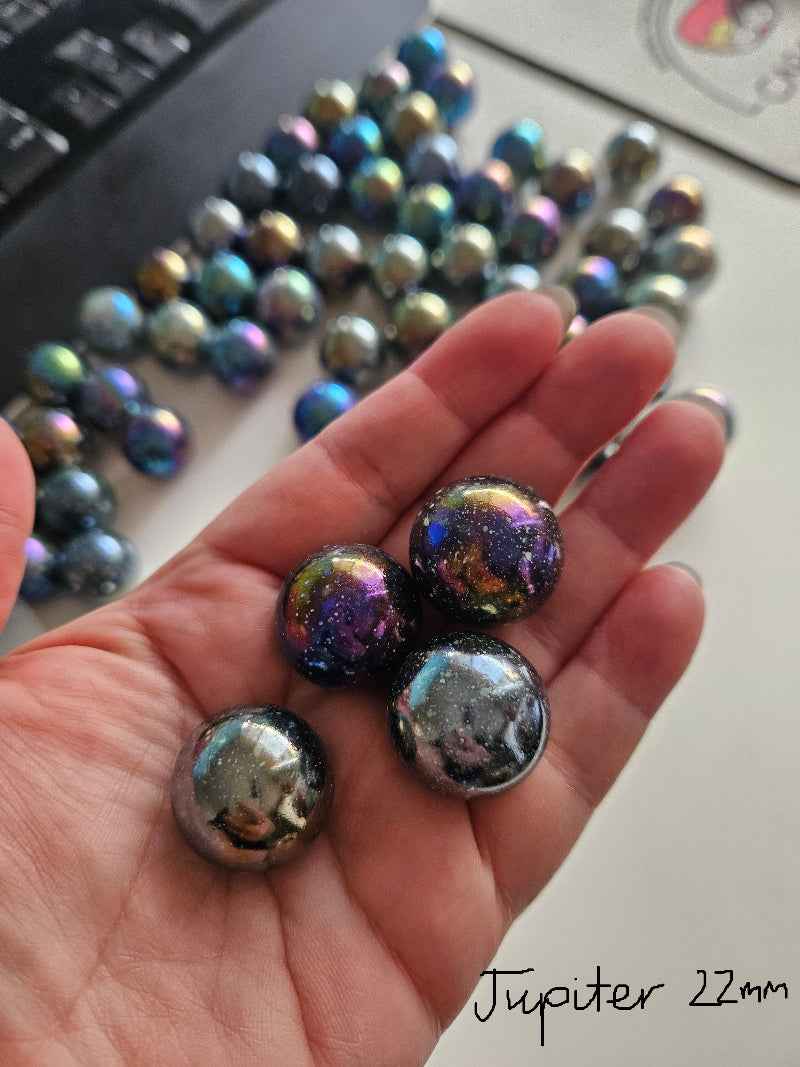 Hand holding iridescent marbles with a laptop in the background