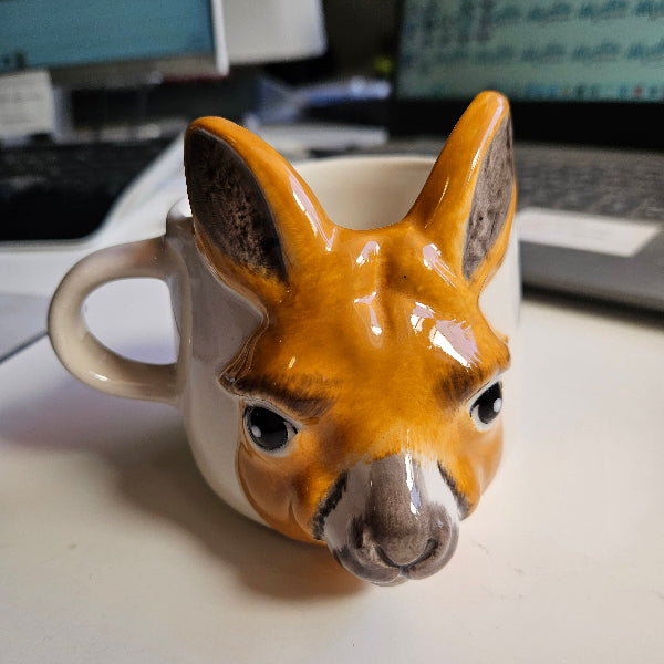Ceramic mug shaped like a kangaroo with a handle on a white surface.