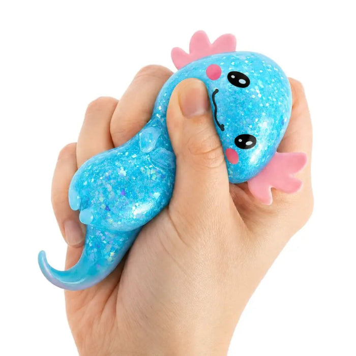Hand squeezing a blue glitter axolotl sensory toy with pink gills and smiling face — Adventure Awaits