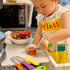 child using kiddie food cutter in kitchen to chop tomato
