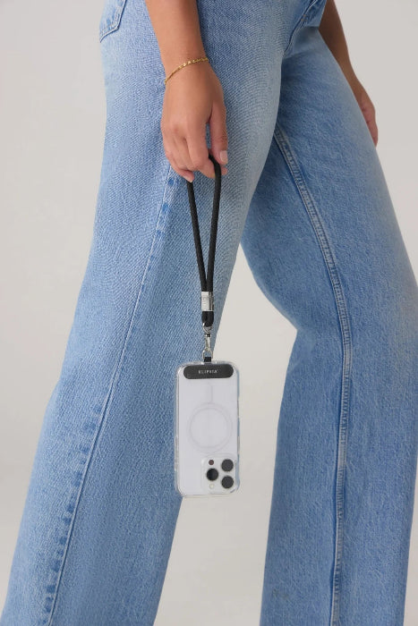 Woman carries a phone by a black wrist strap while wearing blue jeans, Adventure Awaits