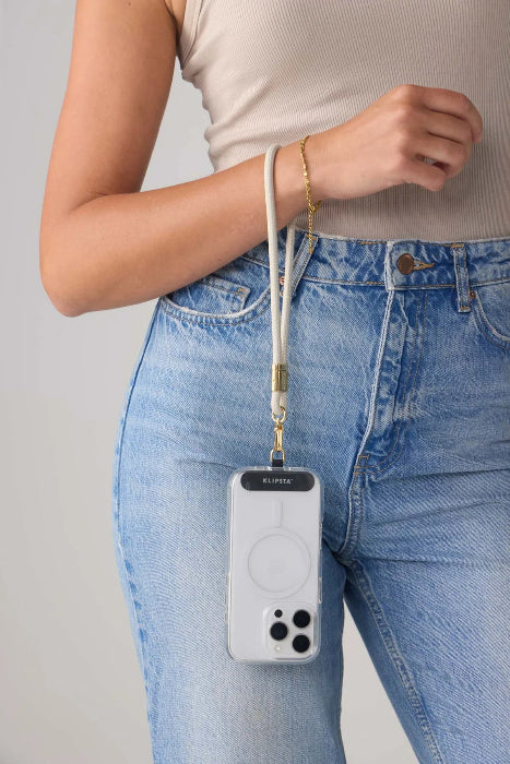 Woman carries a phone from a light grey wrist strap with gold clasp beside blue jeans, Adventure Awaits