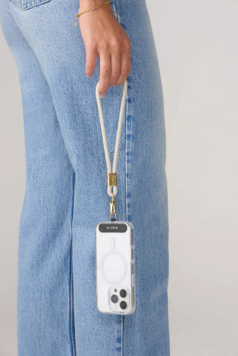 Woman holds a phone by a light grey wrist strap with gold clasp beside blue jeans, Adventure Awaits