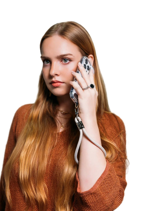 Woman takes a call with her phone secured by a light grey wrist strap with gold clasp, Adventure Awaits