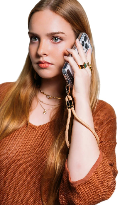 Woman takes a call with her phone secured by a tan wrist strap with gold clasp, Adventure Awaits