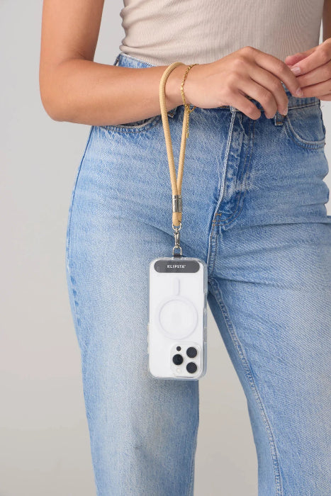 Woman wears a tan phone wrist strap carrying her phone beside blue jeans, Adventure Awaits