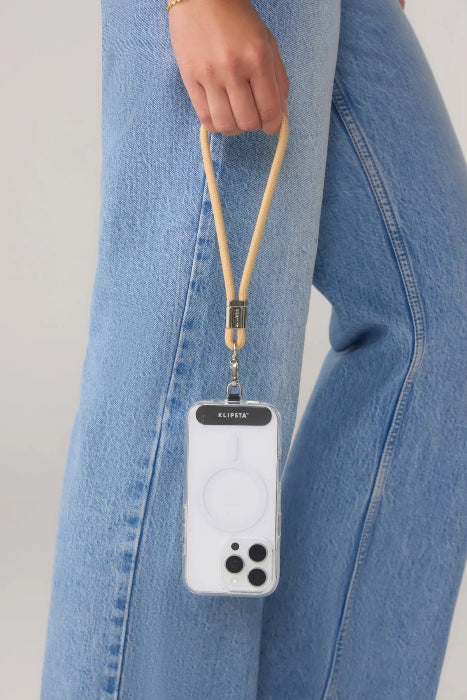 Woman holds a phone by a tan wrist strap beside blue jeans, Adventure Awaits