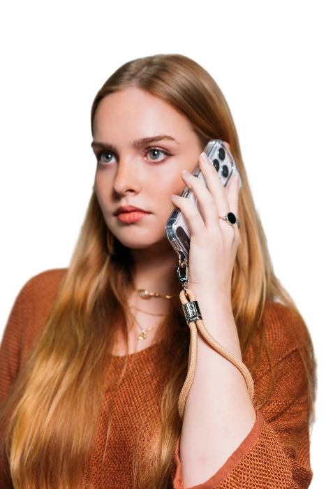 Woman takes a call with her phone secured by a tan wrist strap, Adventure Awaits