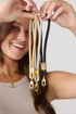 Woman holds beige, grey and black phone wrist straps with gold clasps, Adventure Awaits