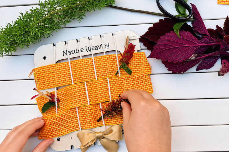child weaving ribbon and florals through square wooden nature weaving frame - Adventure Awaits