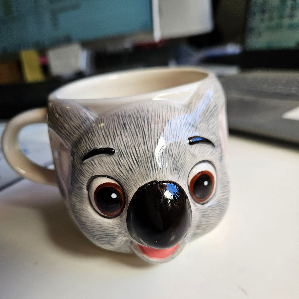 Ceramic mug shaped like a koala with a smiling expression on a white surface.