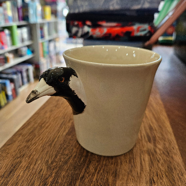 magpie head handle mug on a wooden surface with a blurred background of books and shelves.