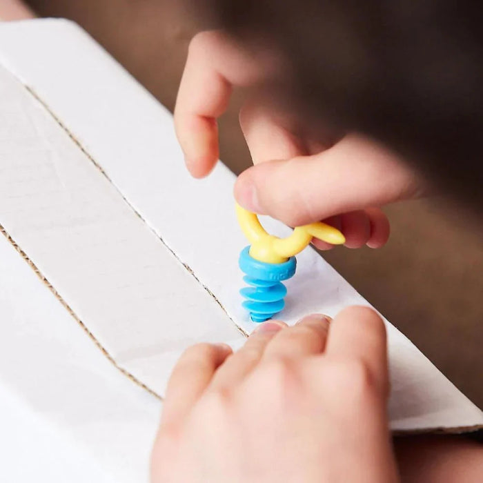 Child twists a yellow Makedo Mini-Tool to secure a blue connector through cardboard — Adventure Awaits