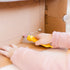 Child uses a yellow Makedo Safe-Saw to cut cardboard horizontally along a drawn line during creative play — Adventure Awaits