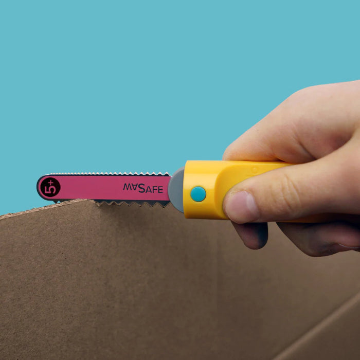Hand uses the yellow Makedo Safe-Saw to cut corrugated cardboard with its child-safe serrated blade — Adventure Awaits