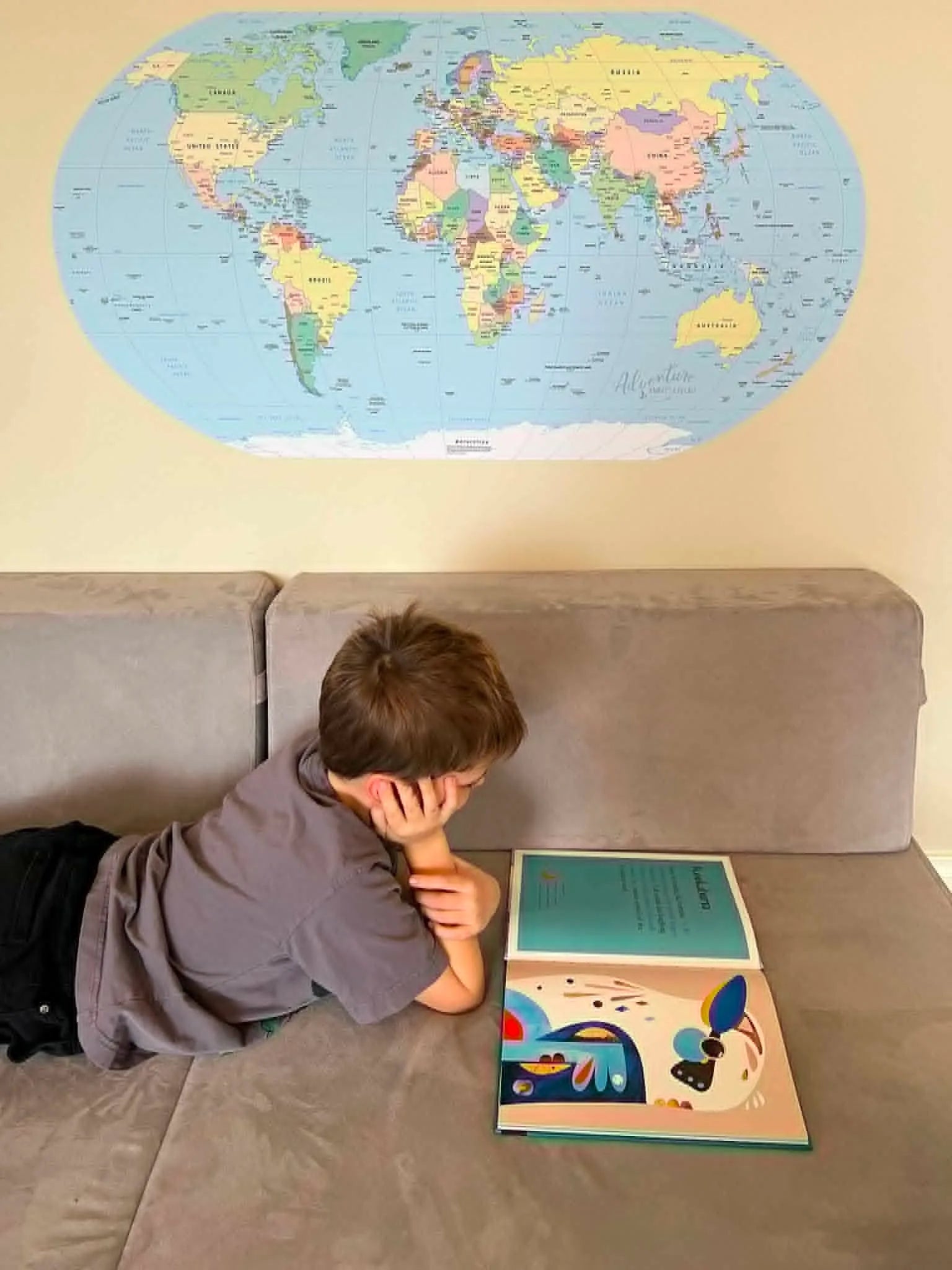 Young boy reading a book with Map of the World sticker on the wall.