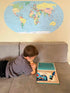 Young boy reading a book with Map of the World sticker on the wall.