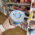 Hand holding a cylindrical product with a blue label in a store setting