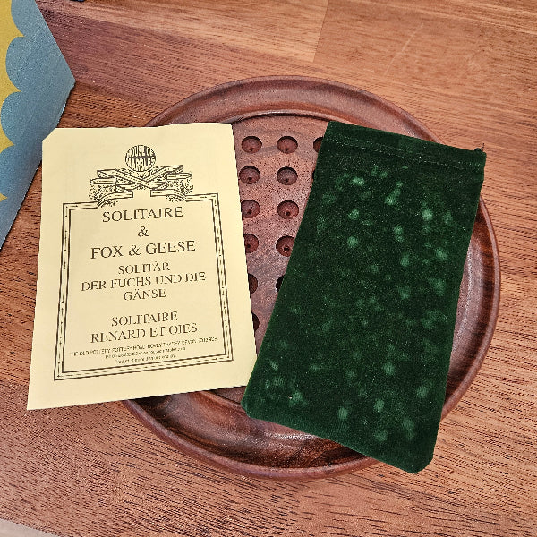 Green pouch on a wooden plate with a paper solitaire instructions on a wooden surface