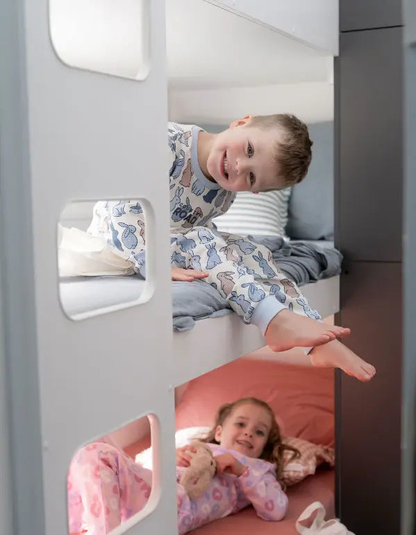 Two children relaxing in caravan bunk beds wearing pyjamas inside a modern family camper interior