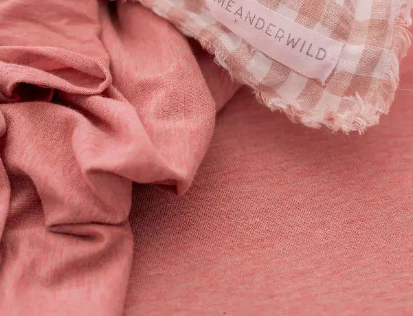 Soft dusty pink fabric with natural folds beside a gingham trimmed Meanderwild textile label