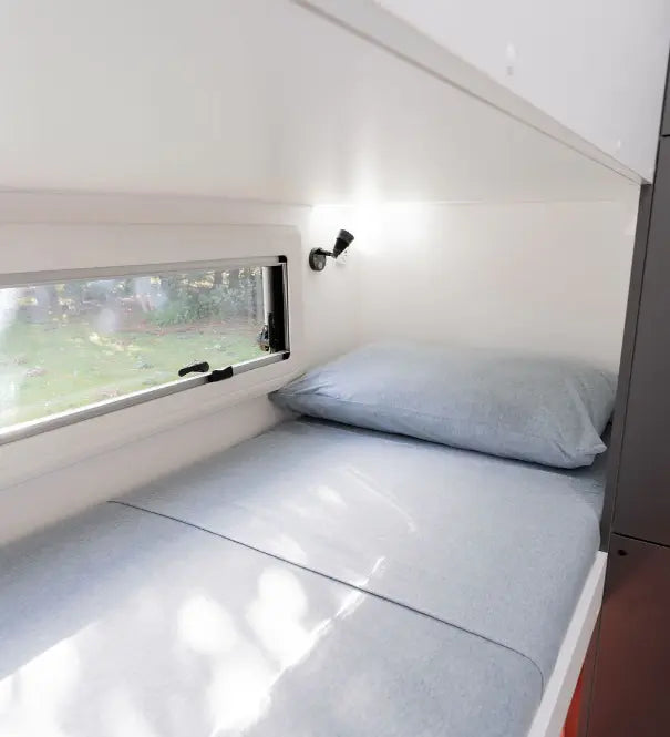 Modern caravan bunk bed with blue bedding, side window and compact family camper interior design
