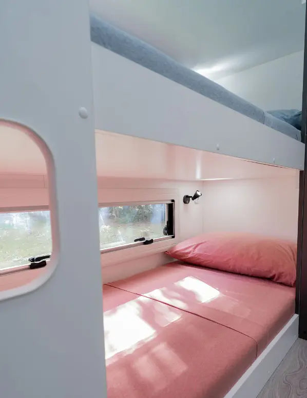 Modern caravan bunk beds with pink bedding, window lighting and compact family travel interior design