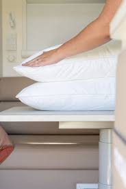 Hands placed on two stacked white pillows on a table, clean and comfortable bedding setup for travel Adventure Awaits