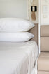 Two stacked white pillows on neatly made bed beside caravan wall, clean and comfortable bedding setup for travel Adventure Awaits