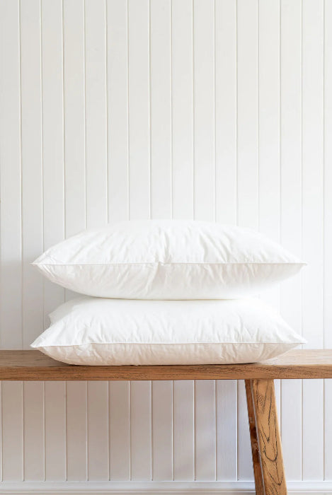 Two stacked white pillows on wooden bench against panelled wall, simple clean bedding display for home or travel comfort Adventure Awaits