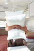 Person holding three white pillows inside caravan, showcasing soft comfortable bedding ideal for travel and compact living Adventure Awaits