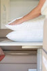 Hands placed on two stacked white pillows on a table, clean and comfortable bedding setup for travel Adventure Awaits