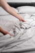 Hand smoothing MeanderWild driftwood flannelette sheet on a caravan queen bed — premium caravanning bedding — Adventure Awaits