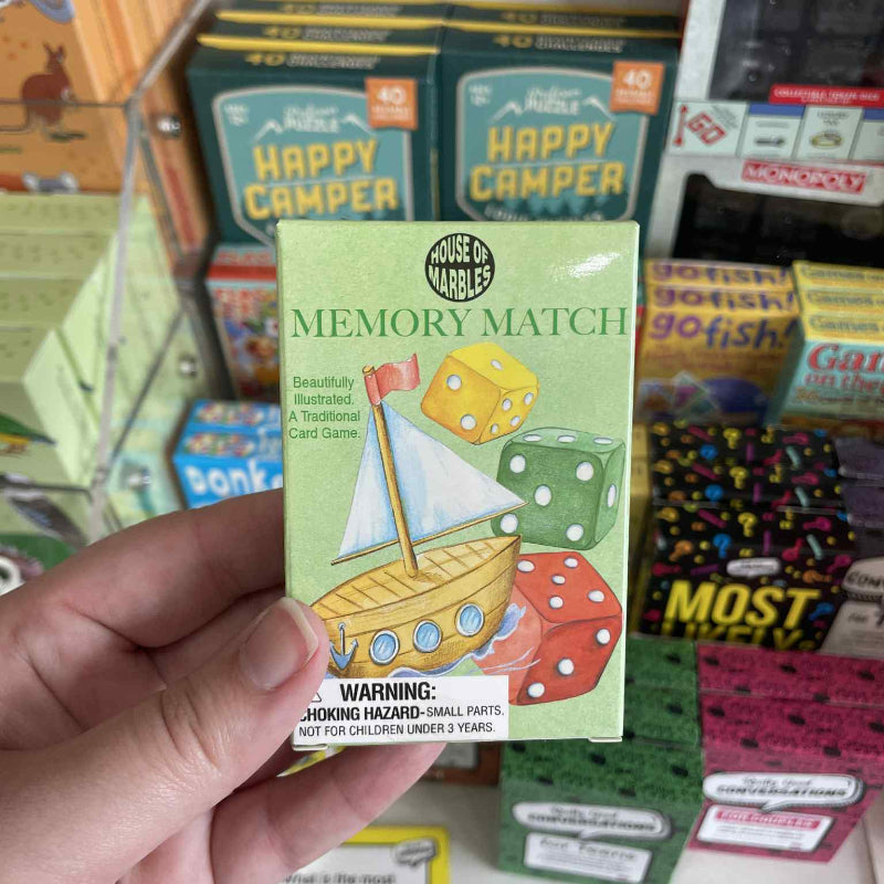 Hand holding a 'Memory Match' game box with colorful packaging in a store setting.
