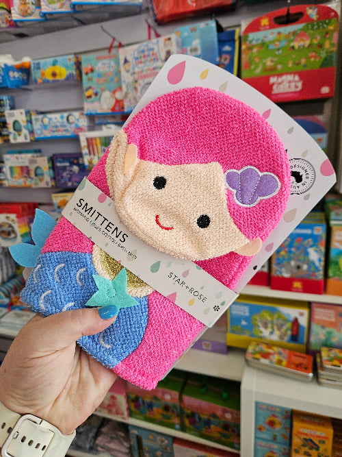 Pink and blue mittens with a cartoon character held in front of a bookshelf.