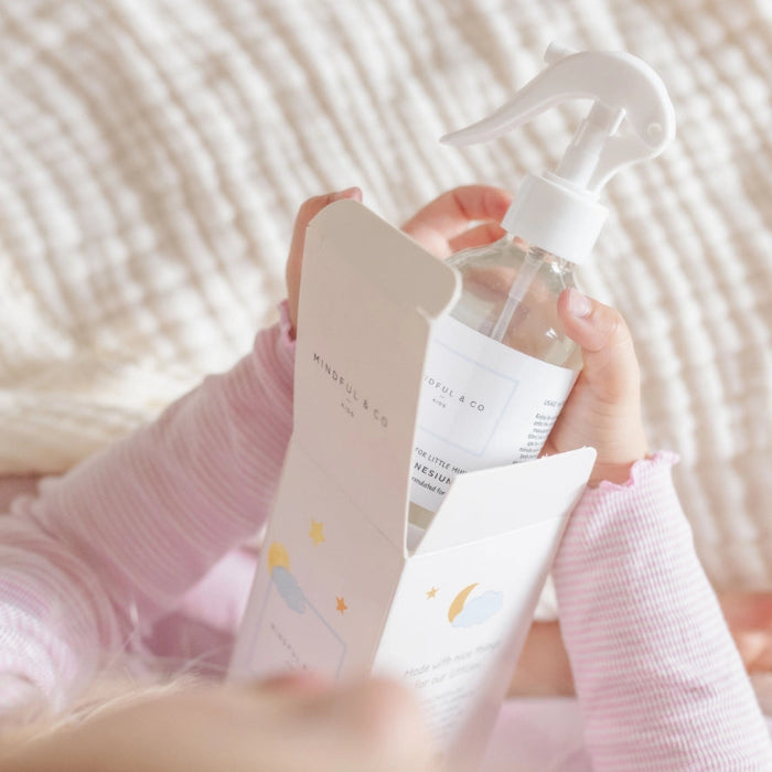 Child holding Mindful and Co calming magnesium oil spray bottle taken from packaging, gentle sleep support for babies and children at home or travel Adventure Awaits